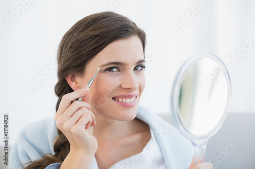 Happy casual brown haired woman in white pajamas plucking her ey photo