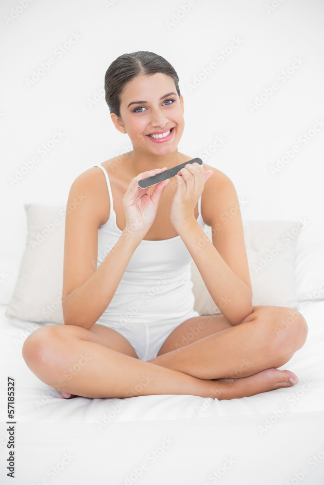 Cute young brown haired model in white pajamas filing her nails Cute young brown haired model in white pajamas filing her nails
