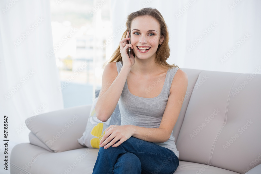 Happy young woman sitting on couch talking on smartphone Happy young woman sitting on couch talking on smartphone