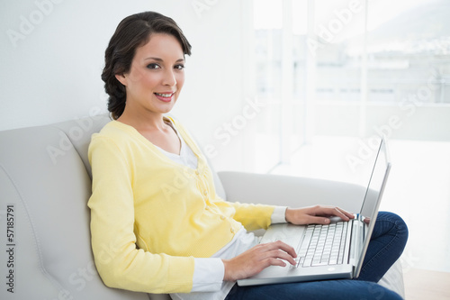 Charming casual brunette in yellow cardigan using a laptop