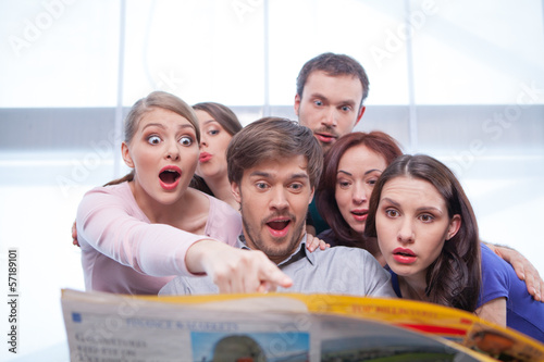 Group of young people reading newspaper.