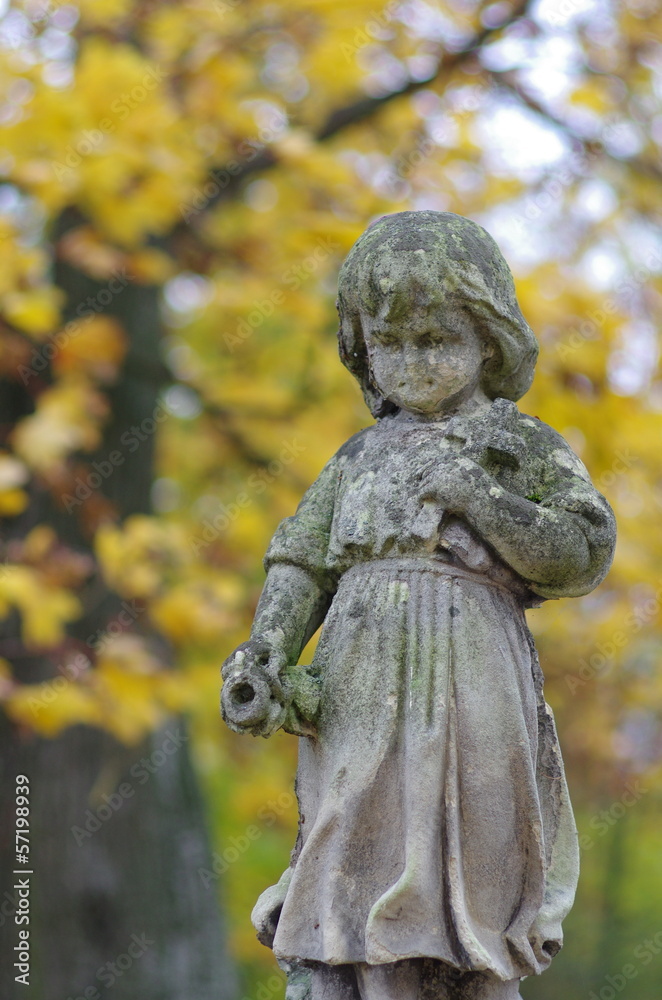 Figura dziecka z krzyżem na cmentarzu na tle jesiennych liści Figura dziecka z krzyżem na cmentarzu na tle jesiennych liści
