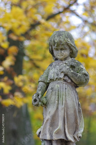Figura dziecka z krzyżem na cmentarzu na tle jesiennych liści © nestonik