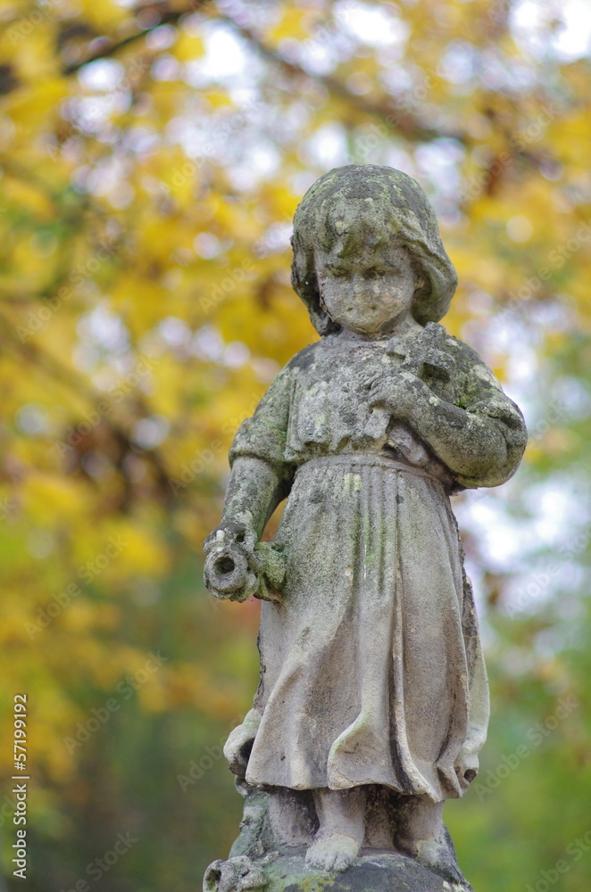 Figura dziecka z krzyżem na cmentarzu na tle jesiennych liści