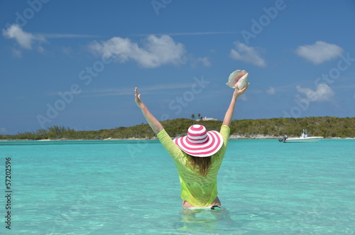 Girl with a seashell in the turqouise water of Atlantic. Exuma,
