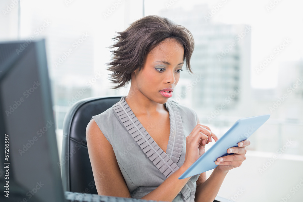 Frowning businesswoman sitting at desk holding tablet pc