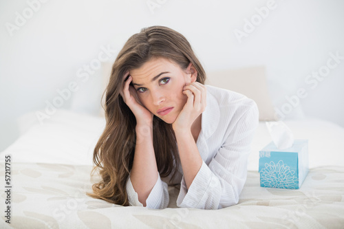 Depressed casual brown haired woman in white pajamas lying on he