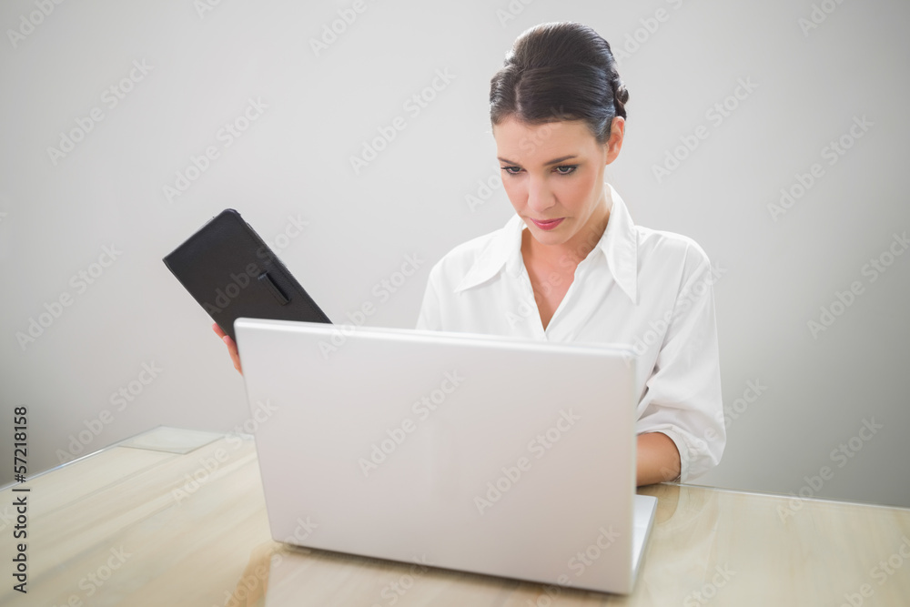 Focused businesswoman working on laptop holding datebook Focused businesswoman working on laptop holding datebook
