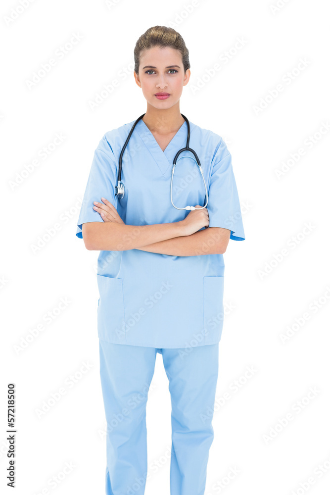 Serious brown haired nurse in blue scrubs posing with arms folde Serious brown haired nurse in blue scrubs posing with arms folde