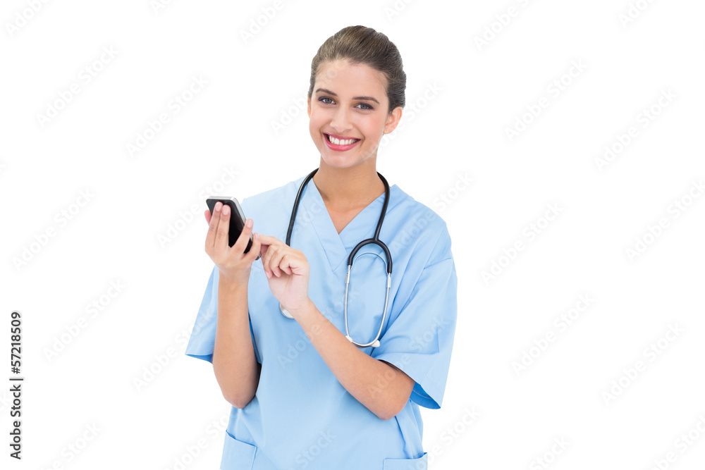 Pleased brown haired nurse in blue scrubs using a mobile phone Pleased brown haired nurse in blue scrubs using a mobile phone