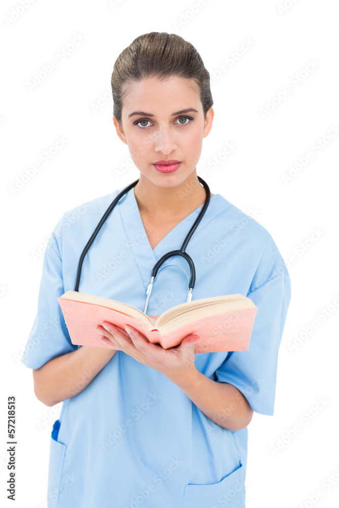 Stern brown haired nurse in blue scrubs holding a book Stern brown haired nurse in blue scrubs holding a book