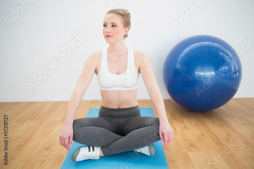 Content sporty blonde sitting cross legged on exercise mat