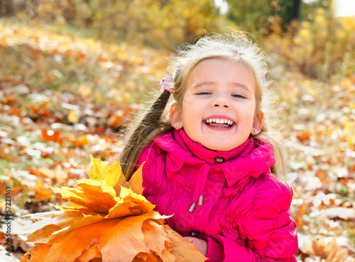 Autumn portrait of cute laughing little girl with maple leaves