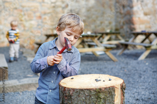 Little blond boy playing with hammer outdoors with brother.