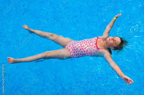 Child girl laying on the swimming pool water surface