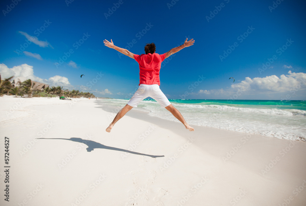 Young man jumping and raising his arms up on the beach