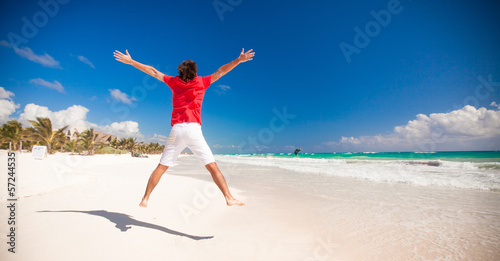 Young man jumping and raising his arms up on the beach