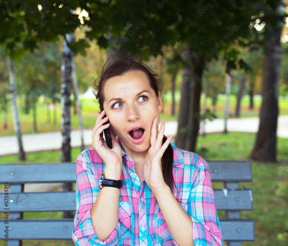 Fototapeta premium Portrait of surprised woman in the park talking on the phone