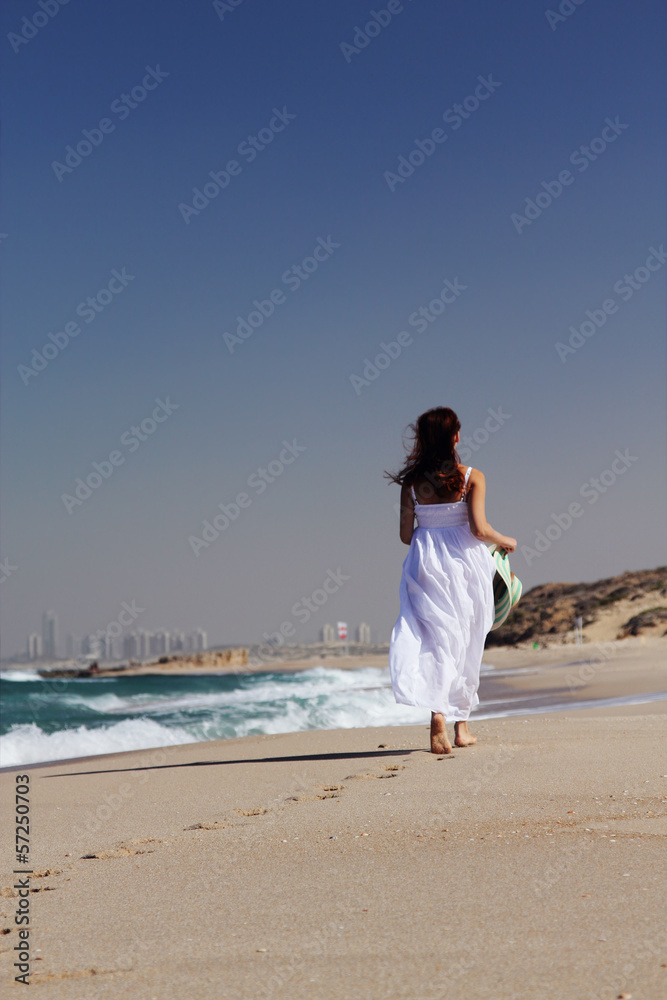 Young woman in white dress walking at the beach. Focus on the sa