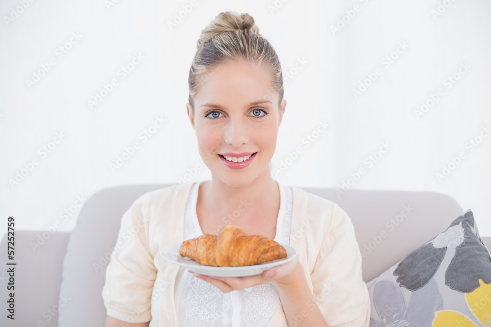 Happy fresh model holding croissant sitting on sofa