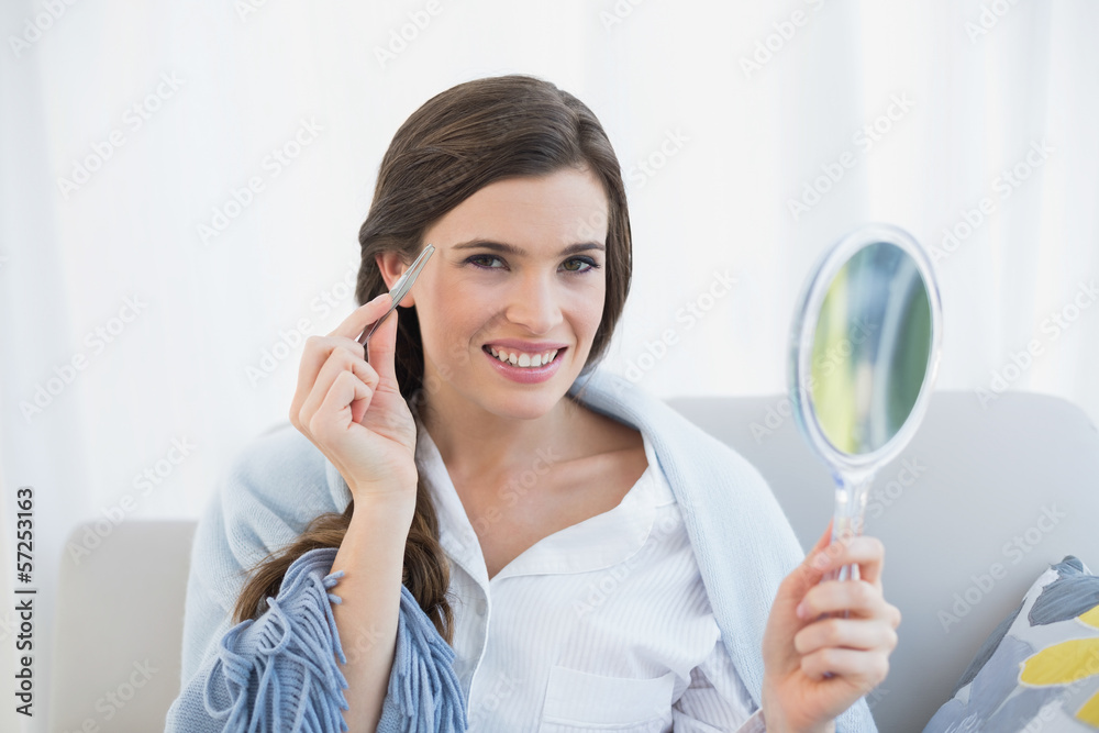 Smiling casual brown haired woman in white pajamas plucking her Smiling casual brown haired woman in white pajamas plucking her