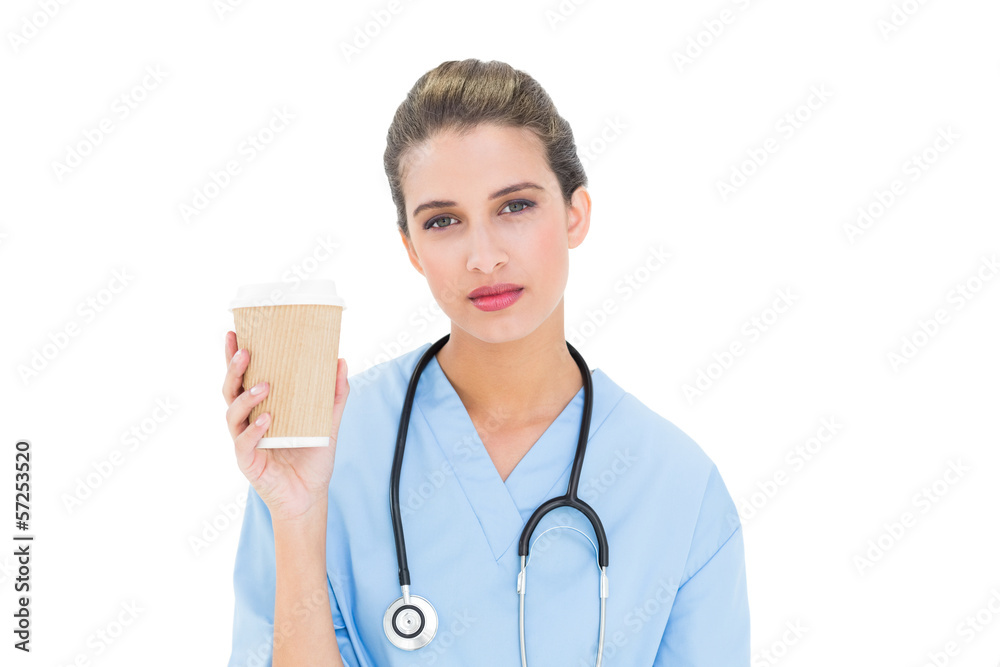 Thoughtful brown haired nurse in blue scrubs holding a cup of co Thoughtful brown haired nurse in blue scrubs holding a cup of co
