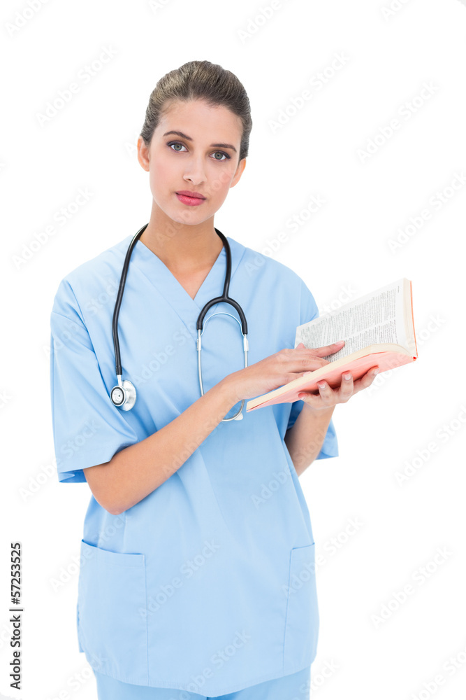 Serious brown haired nurse in blue scrubs holding a book Serious brown haired nurse in blue scrubs holding a book
