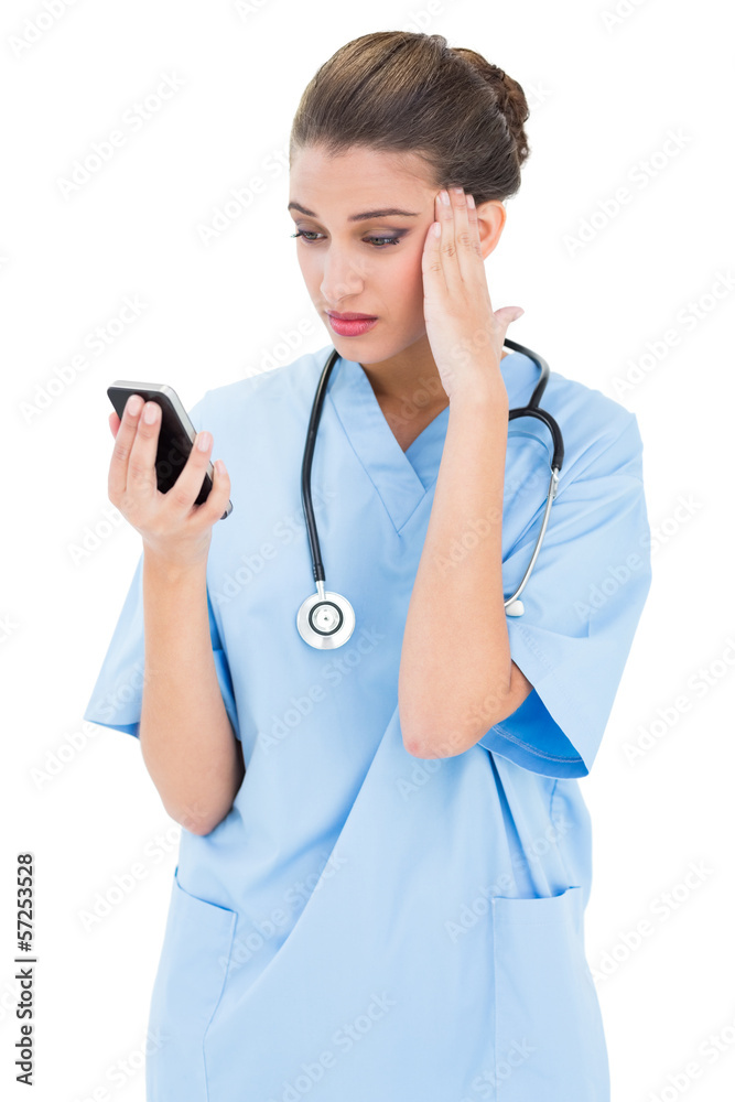 Puzzled brown haired nurse in blue scrubs using a mobile phone Puzzled brown haired nurse in blue scrubs using a mobile phone