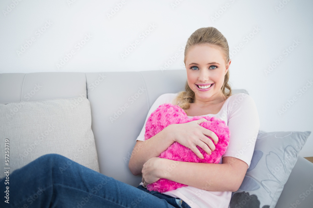 Casual smiling blonde holding heart pillow Casual smiling blonde holding heart pillow
