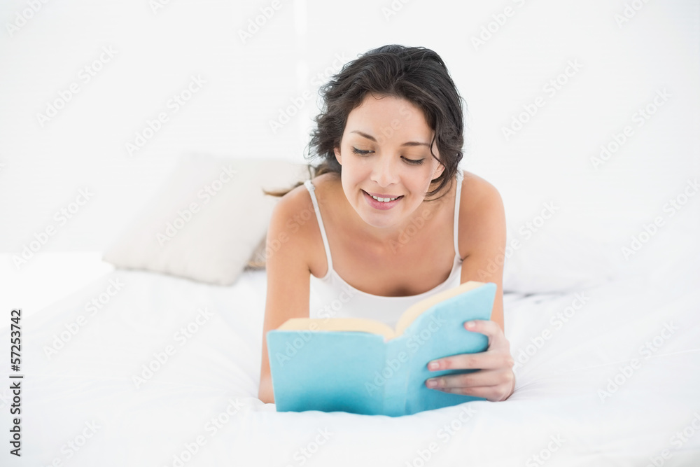 Charming casual brunette in white pajamas lying on her bed readi Charming casual brunette in white pajamas lying on her bed readi