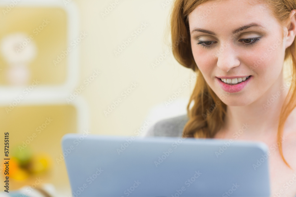Cheerful redhead sitting on the couch using tablet pc Cheerful redhead sitting on the couch using tablet pc