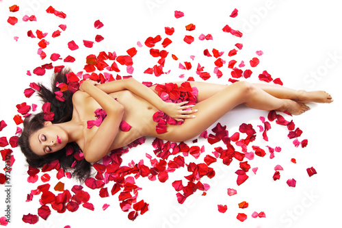 slim woman lying on red roses petals over white