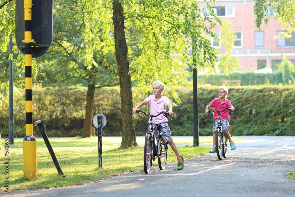 Obraz premium Two twin brothers riding bicycles stopping at red lights