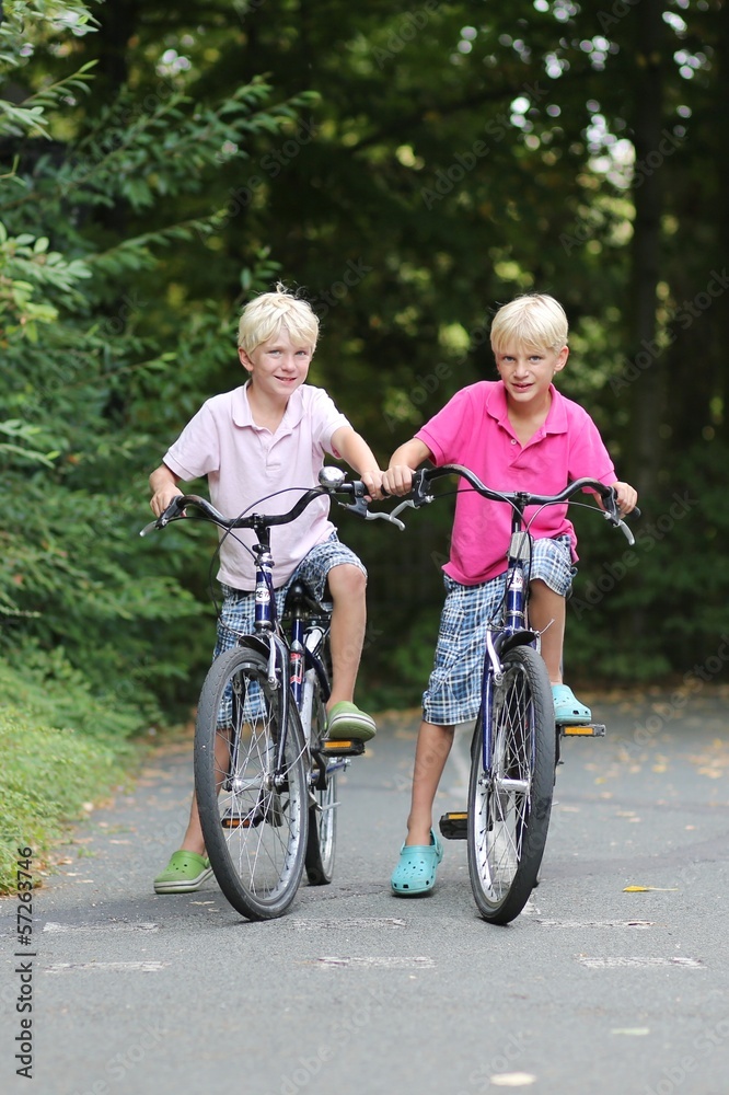 Two teenagers boys, twin brothers are cycling in the park Two teenagers boys, twin brothers are cycling in the park