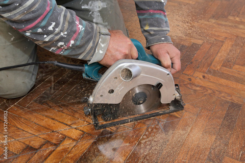 Home renovation worker cut old parquet floor with electric saw