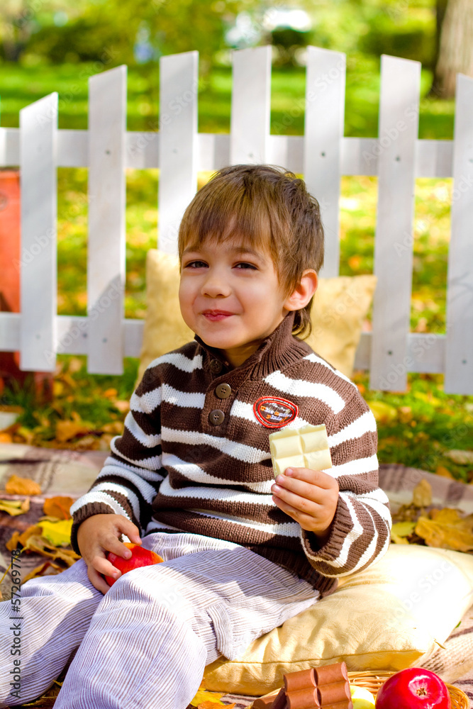 Happy little boy eating chocolate in the autumn forest
