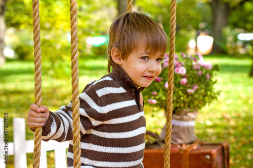 Little boy sitting on a swing in the autumn park