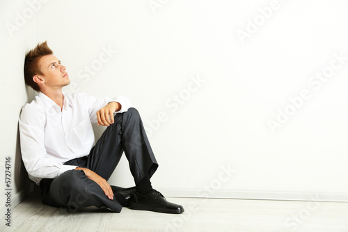 Young businessman  sitting on floor, on gray wall background