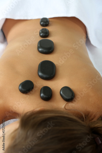 Beautiful young woman having stone massage in spa salon
