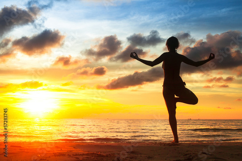 Silhouette of young woman practicing yoga on the beach