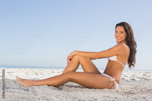 Cheerful attractive brunette in white bikini posing while sittin