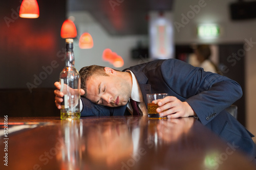 Unmoving businessman holding whiskey glass lying on a counter