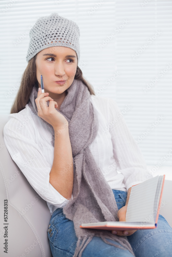 Pensive pretty brunette with winter hat on holding notebook Pensive pretty brunette with winter hat on holding notebook
