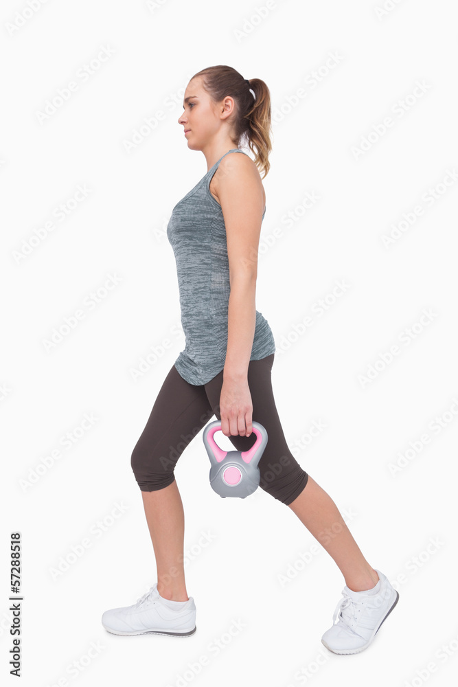 Sporty woman training her body walking with a kettle bell