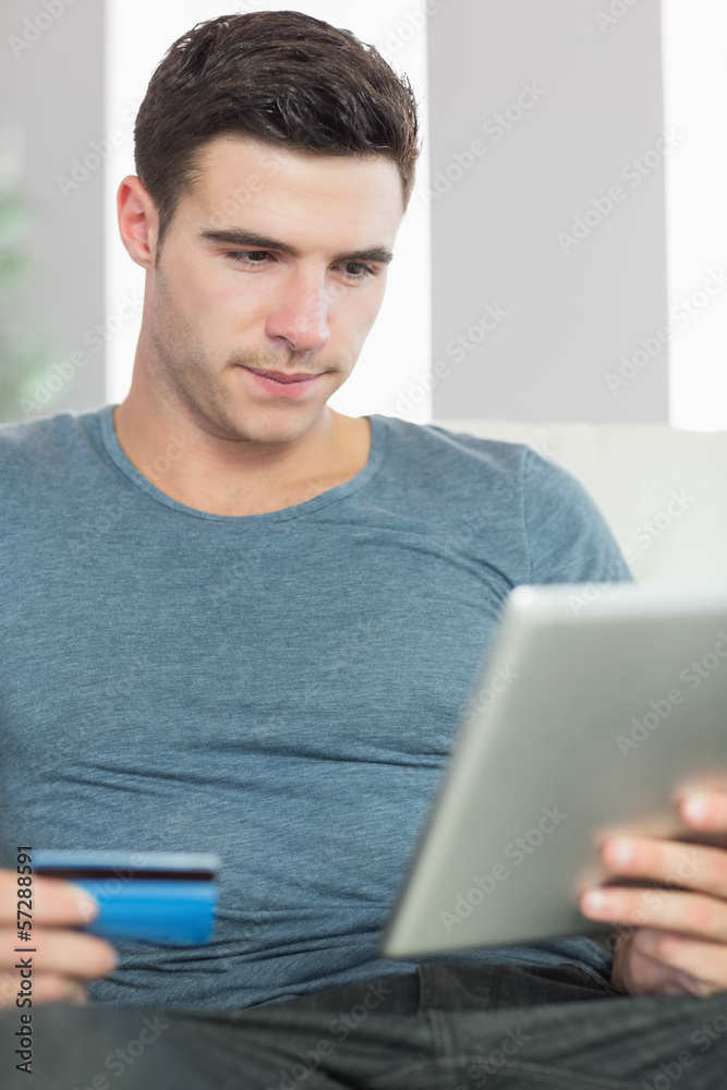 Content handsome man relaxing on couch using tablet shopping onl Content handsome man relaxing on couch using tablet shopping onl