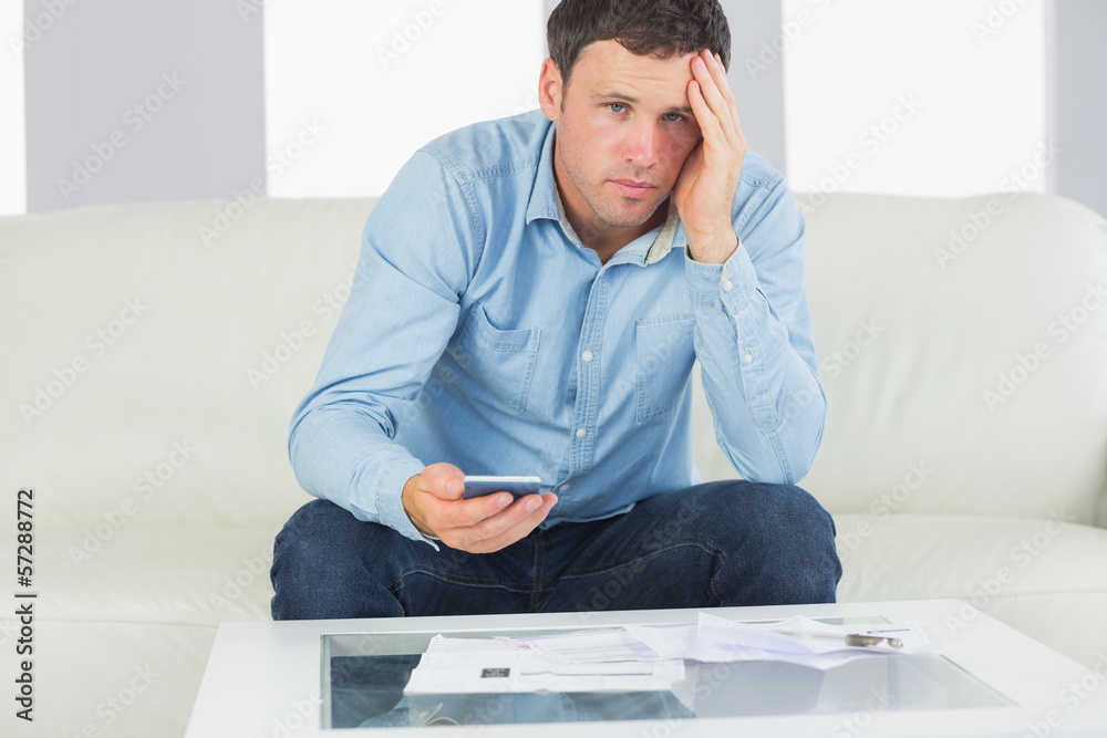 Upset casual man using calculator and looking at camera paying b