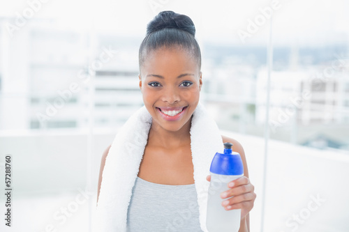 Fit smiling woman with towel around her neck holding sports bott Free Download Fit smiling woman with towel around her neck holding sports bott - GFXLoad