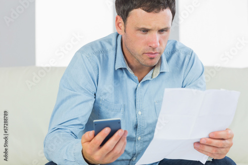 Serious casual man holding calculator paying bills looking at do