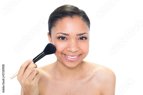 Delighted young dark haired model applying powder on her cheeks