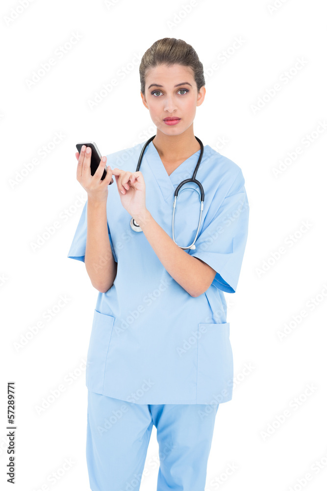 Surprised brown haired nurse in blue scrubs using a mobile phone Surprised brown haired nurse in blue scrubs using a mobile phone